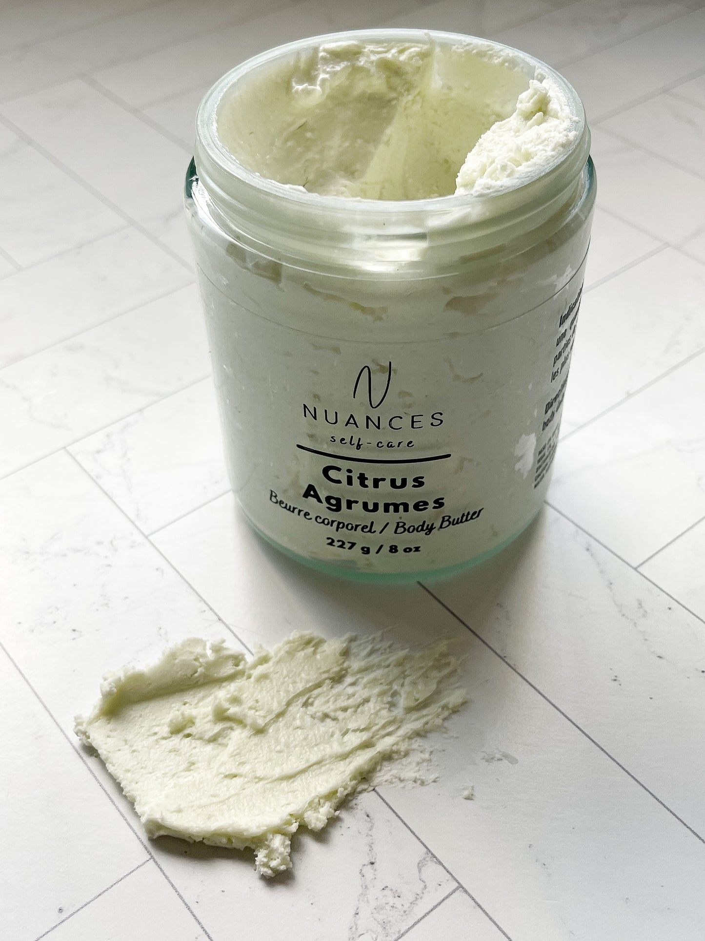 The citrus body butter cream on a white tile floor