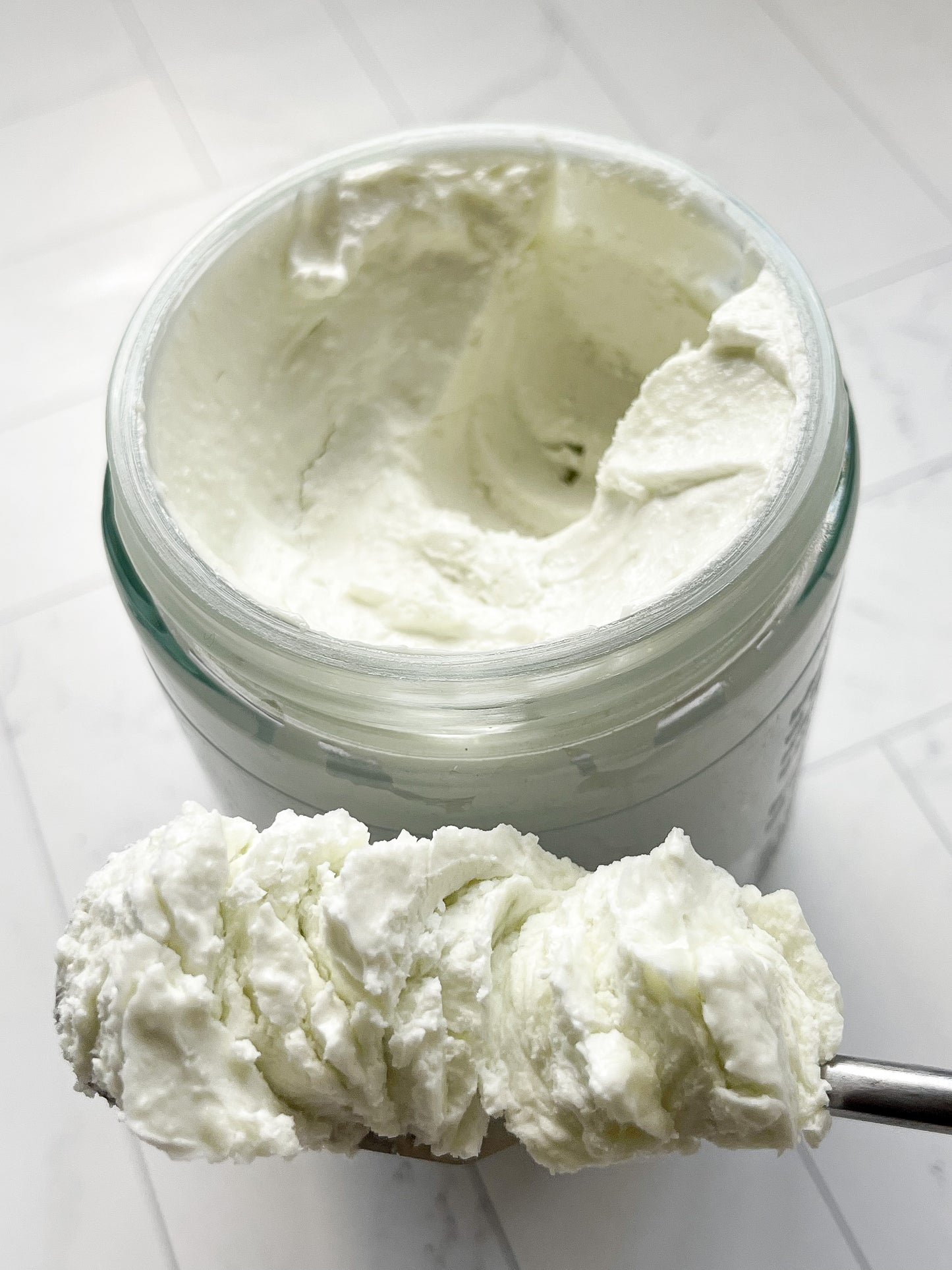 An open jar of the citrus body butter with a spoonful of the body butter to show the consistence.