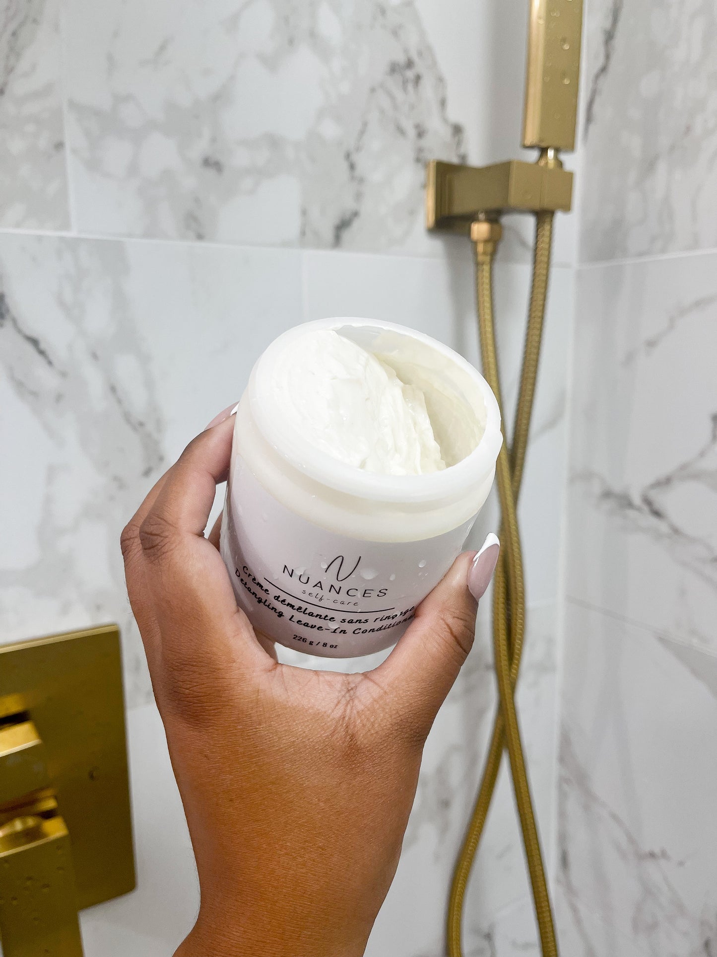 An open jar of the leave-in conditioner shown in the shower